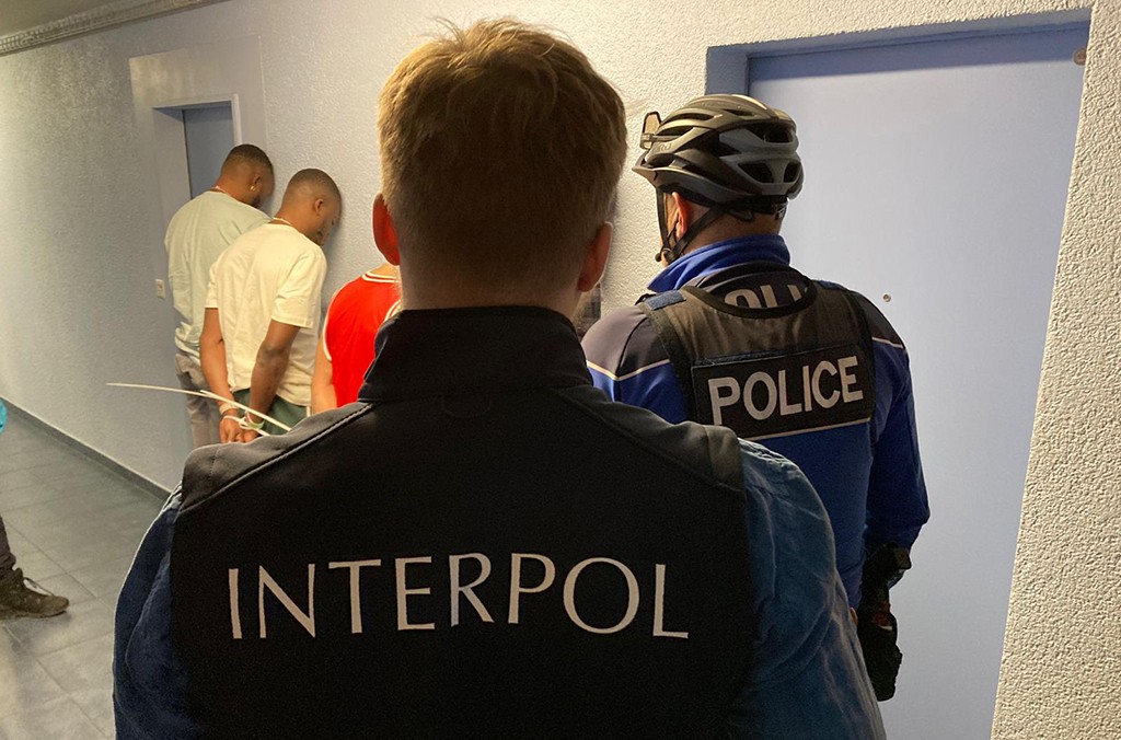Interpol and police officers detaining suspects during international fraud crackdown arrests